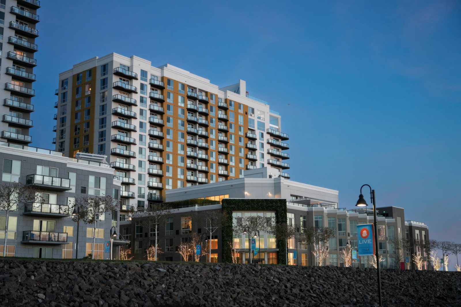 Ground-level view of a finished apartment community at dusk, walkways swept and landscaping watered, warm light in the windows and the leasing office door standing open.