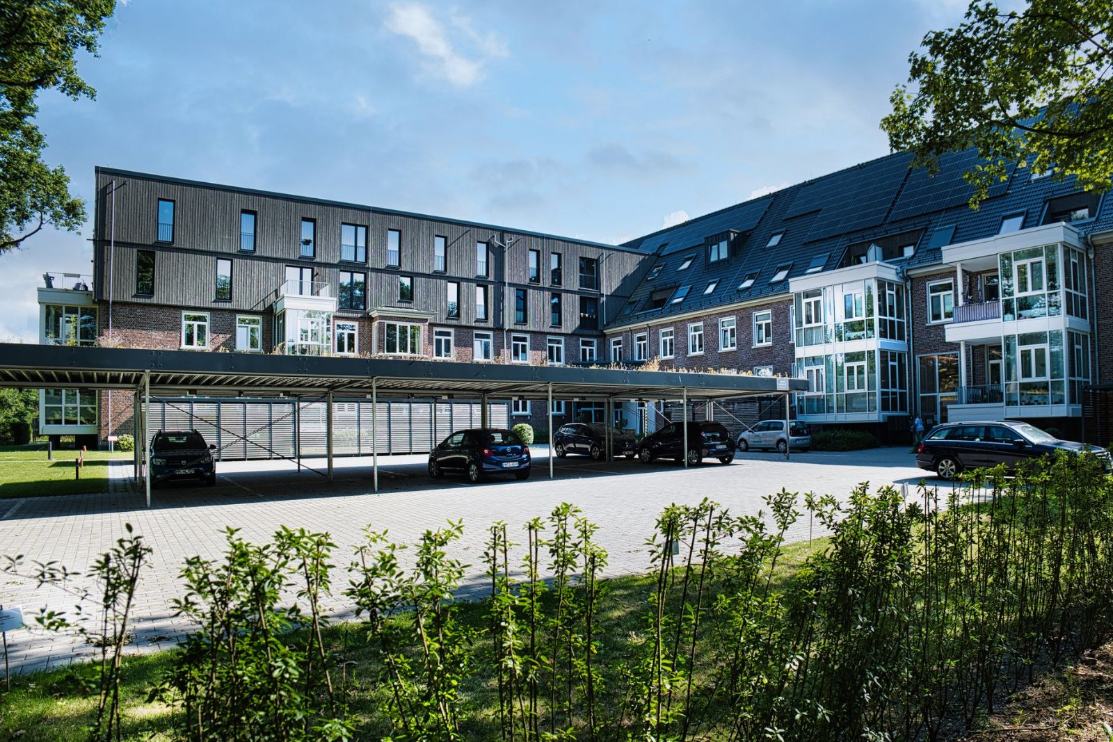 A two- and three-story garden-style apartment community shot low from the parking lot in late-afternoon light, new composition shingle roof planes and crisp ridge line set against open Texas sky, resident cars parked and chairs out on the balconies.